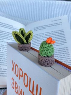 two small crocheted cactus sitting on top of a book with an orange flower