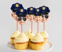 cupcakes with police hats and sunglasses are on a white plate, surrounded by little boys'faces