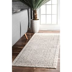 a white rug on top of a wooden floor next to a couch and potted plant