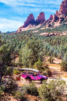 a pink jeep is parked in front of red rocks and trees with mountains in the background