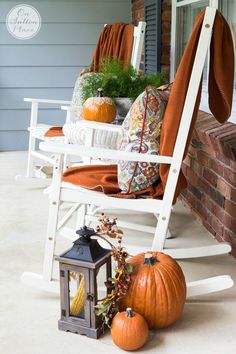 a porch decorated for fall with white rocking chairs and pumpkins