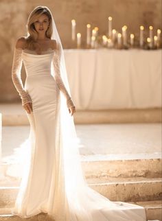 a woman in a wedding dress standing on steps with candles behind her and looking at the camera