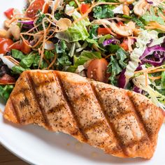 a white plate topped with a salad and meat on top of a bed of lettuce