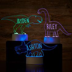 two illuminated dinosaurs on pedestals with name and date in blue, green, yellow or pink