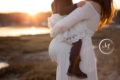 a woman holding a baby in her arms while standing next to a body of water