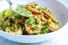 a white bowl filled with shrimp and broccoli covered in sauce next to a lime wedge