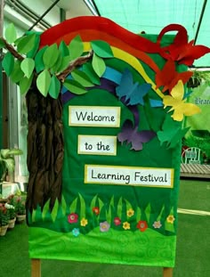 a welcome to the learning festival sign with paper flowers and leaves on it in a greenhouse