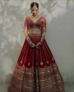 a woman in a red and gold lehenga standing next to a white wall