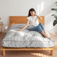 a woman sitting on top of a bed next to a plant