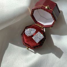 two red jewelry boxes sitting on top of a white cloth