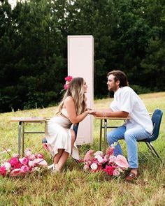 a man and woman sitting at a table with flowers on the ground in front of them