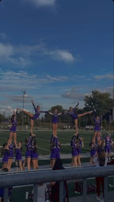 a group of cheerleaders standing on top of a metal railing in front of a football field