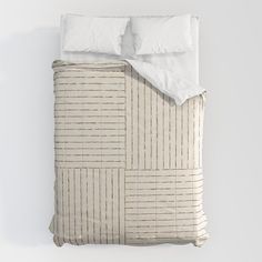 a bed with two pillows and a white comforter on top of it in front of a wall