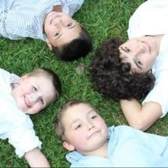 four children laying in the grass with their heads on each other's shoulders and looking up at the camera