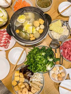 a table full of food including meats, noodles and vegetables with chopsticks