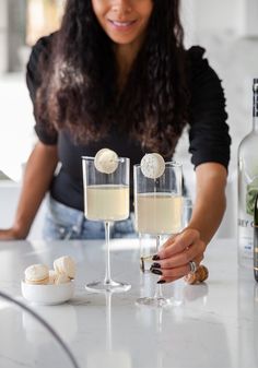 a woman sitting at a table with two glasses of wine in front of her and another glass on the counter