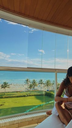 a woman sitting on top of a bed next to a window looking out at the ocean