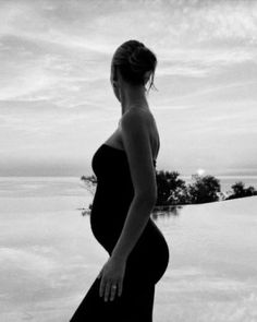 a pregnant woman standing in front of a swimming pool with the sun setting behind her