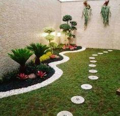 an outdoor garden with stepping stones and plants on the grass, along side a white brick wall