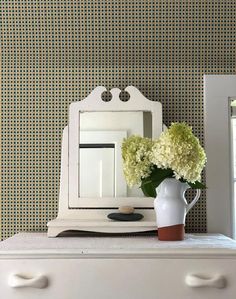 a white dresser topped with a vase filled with flowers next to a wall mounted mirror