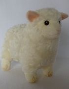 a white stuffed sheep is standing on a white surface with its head turned to the side