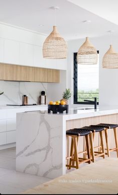 a kitchen with white cabinets and gold bar stools on the island in front of it