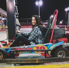 a woman sitting on top of a miniature car at an amusement park in the dark