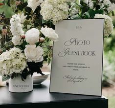 a table topped with white flowers next to a sign that says auto guest book on it