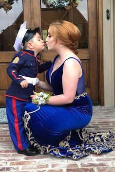 a woman in a blue dress kissing a small child on the cheek while wearing a soldier's uniform