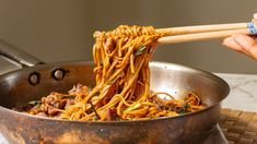 someone is holding chopsticks over noodles in a wok