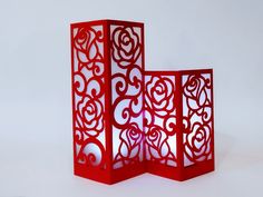 two red vases sitting next to each other on a white surface with an intricate design