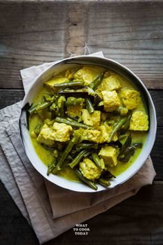 a bowl filled with green beans and tofu in curry sauce on top of a wooden table