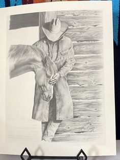 a pencil drawing of a cowboy holding a horse's bridle and standing next to a wooden fence