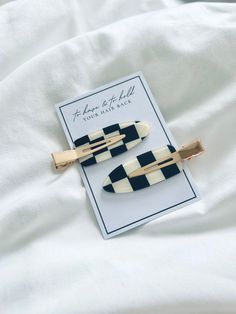 two black and white striped hair clips laying on top of a white sheet with a card