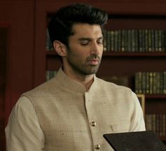 a man standing in front of a bookshelf holding a book and looking at it