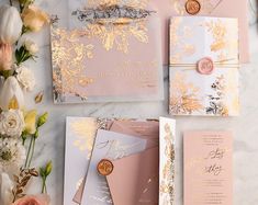 the wedding stationery is laid out on top of some pink and gold paper, along with flowers