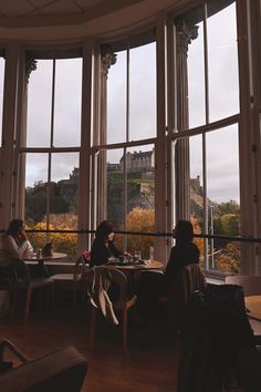 two people sitting at a table in front of large windows looking out onto a castle