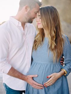 a pregnant couple cuddles and smiles at each other as they stand close together