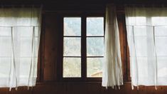 two windows with white curtains in front of them and a mountain view out the window