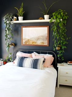 a bed with white sheets, pillows and plants on the wall above it in a bedroom