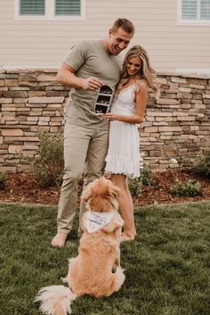 a man and woman standing next to a brown dog on top of a grass covered field