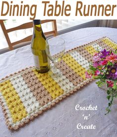 a crocheted table runner with flowers on it and a bottle of wine next to it