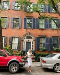 a woman standing next to a red truck in front of a brick building with blue shutters