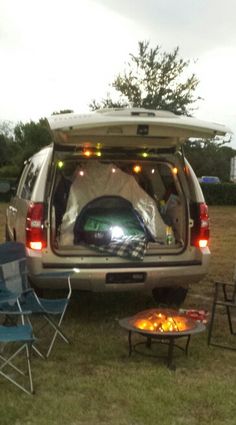 the back end of an suv with its trunk open and camping gear set up outside