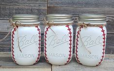 three white mason jars with red stitching and baseballs on them, tied together