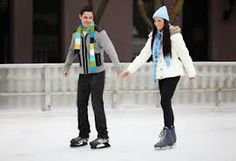 a man and woman holding hands while skating on an ice rink in front of a building