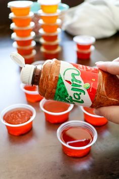 someone is pouring sauce into small cups on a table with orange cups in the background