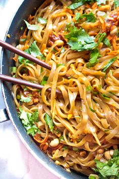 a pan full of noodles with chopsticks and cilantro on the side