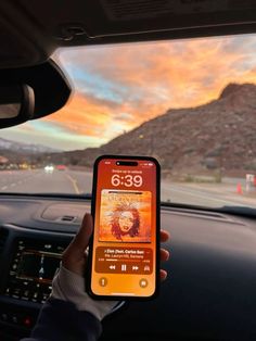 someone is holding up their cell phone while driving down the road with mountains in the background