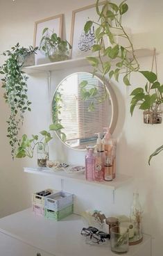 a white dresser topped with plants next to a round mirror and shelves filled with bottles